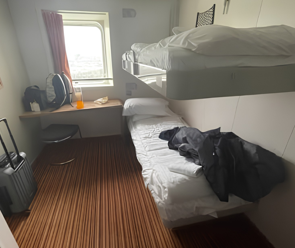 Two-berth ferry cabin with bunk bed, window, small desk and luggage