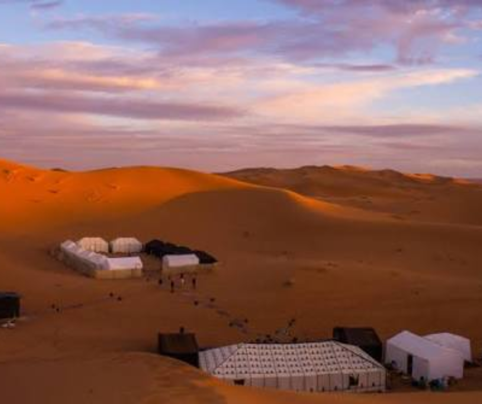 White tents of a desert camp in orange dunes at dusk