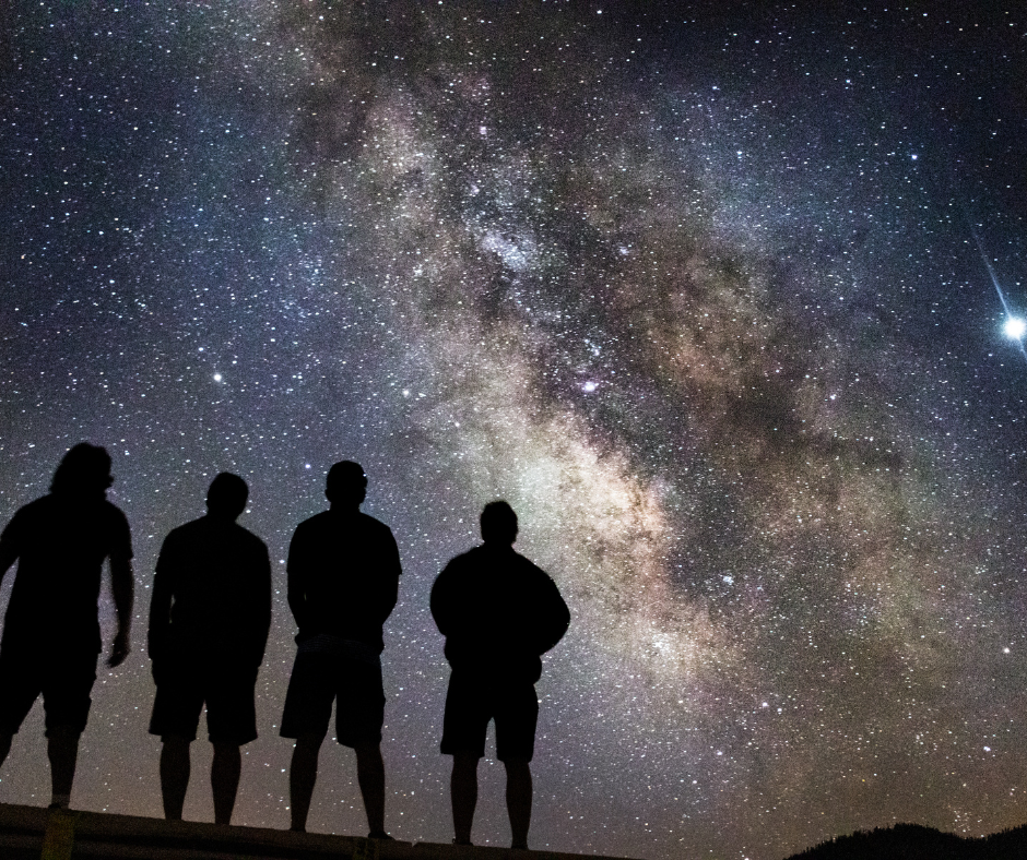 Four silhouetted people looking up at the Milky Way at night