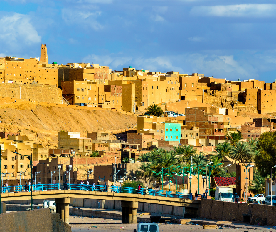 Ochre houses stacked on a hillside above a bridge in the M'Zab Valley