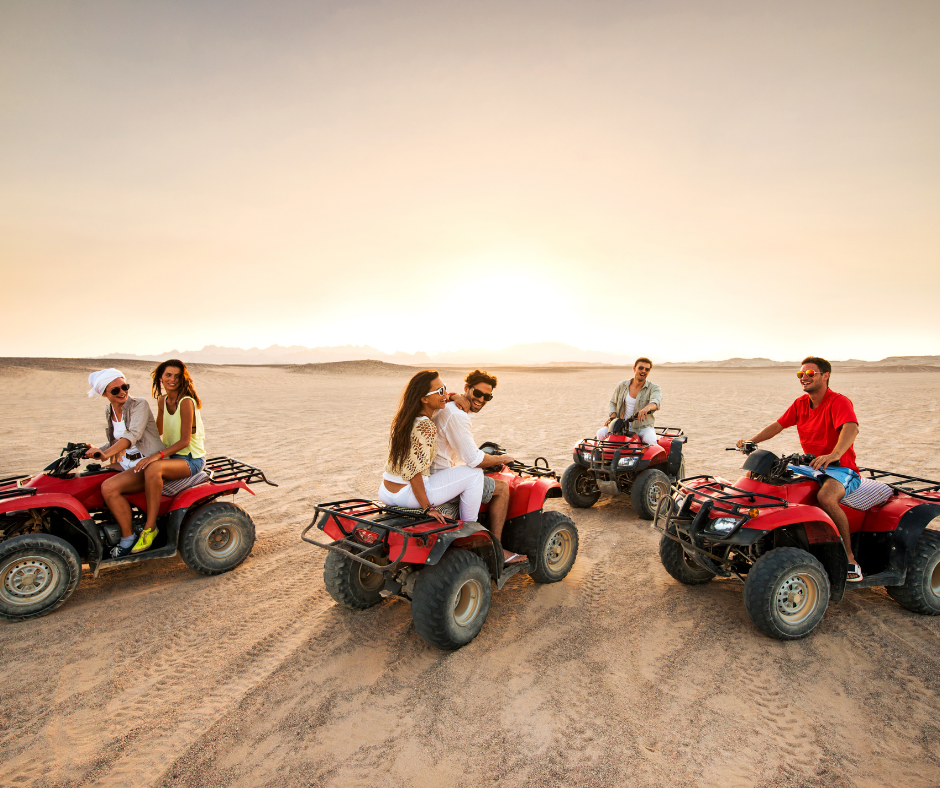 Group riding red quad bikes across sandy desert at sunset