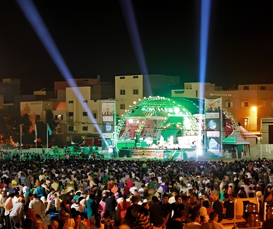 Large night crowd facing a green-lit stage at an open-air festival