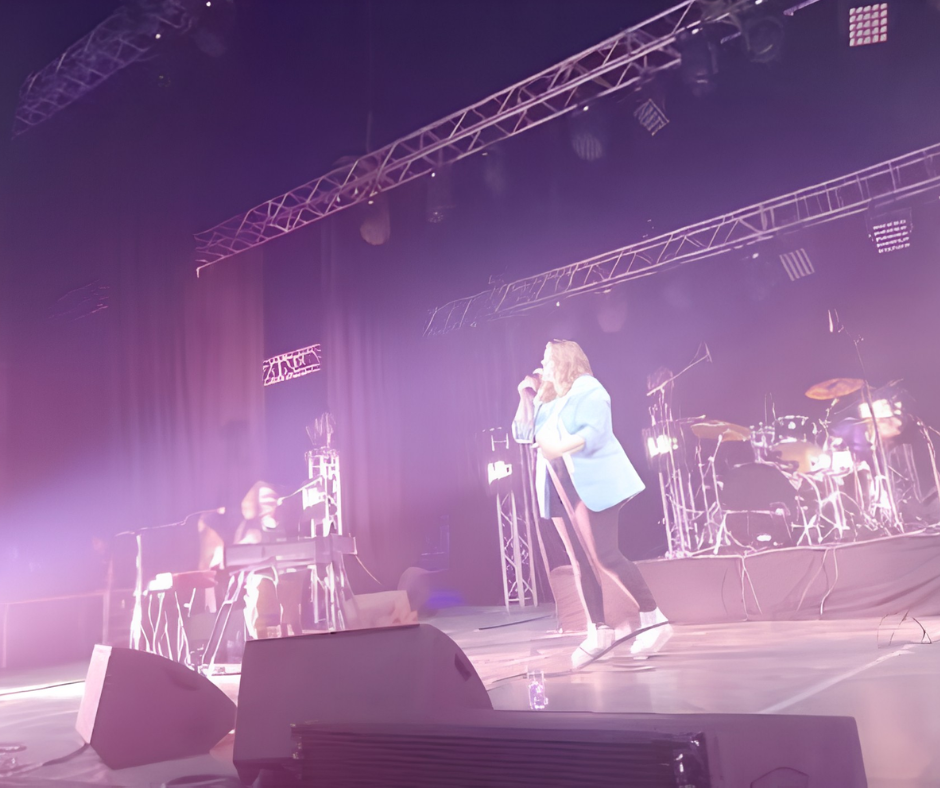 Singer performing on a stage with drum kit and purple lights