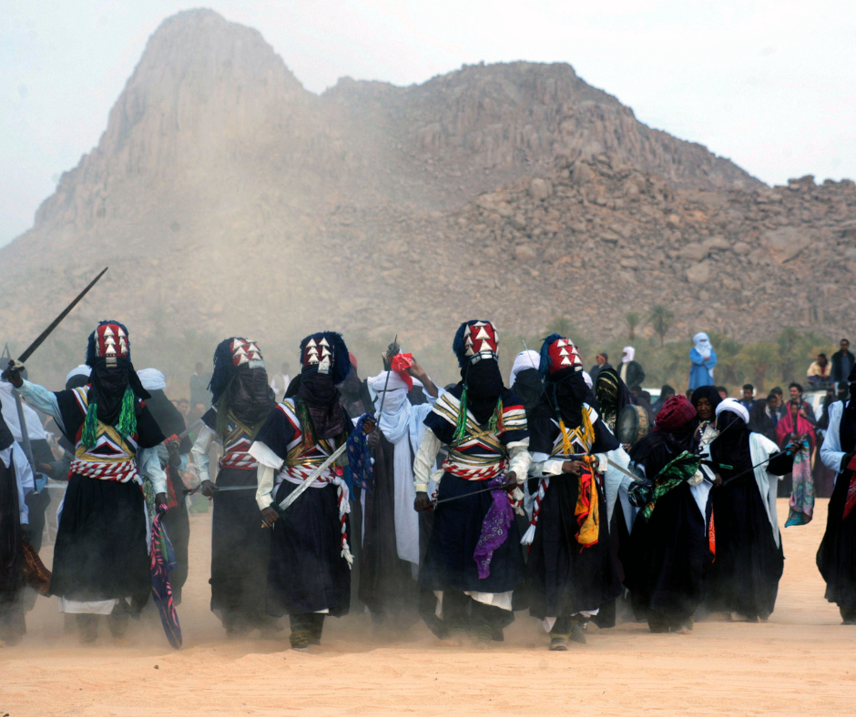 Men in black and white Tuareg dress with swords dancing in a cloud of dust