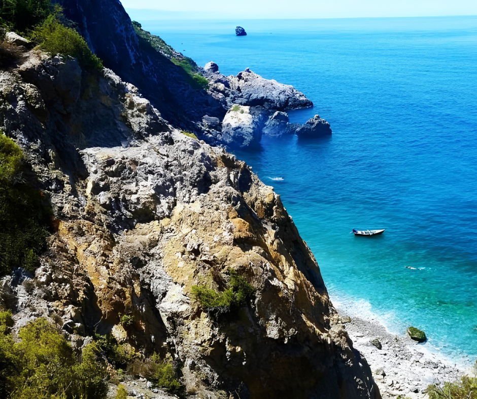 Rocky cliffs above a turquoise cove with a small boat at Cap Blanc