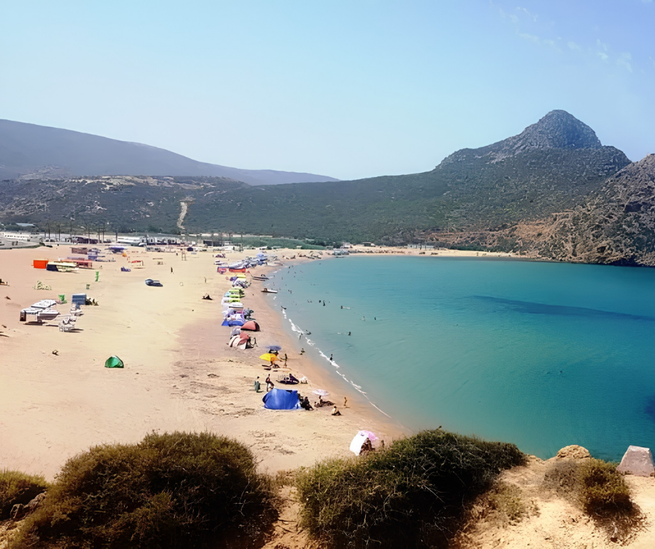 Crowded sandy beach and turquoise bay below a mountain at Madagh