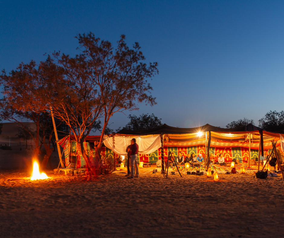 Lit desert camp tent with a campfire in the Sahara at dusk