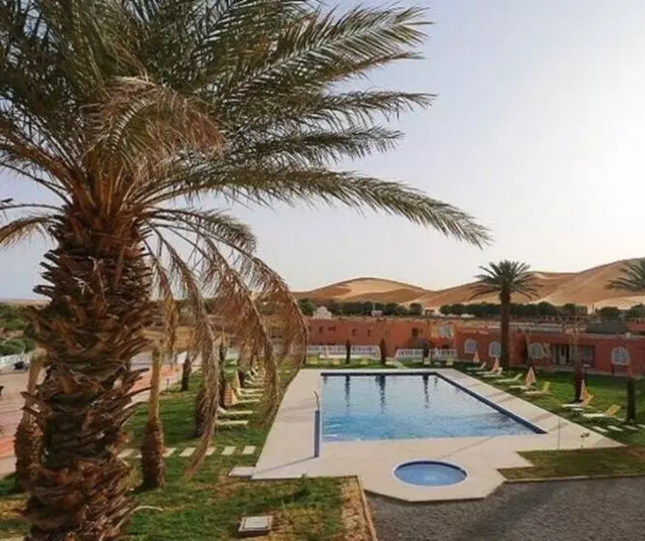 Guesthouse pool and palm trees with sand dunes behind in Taghit