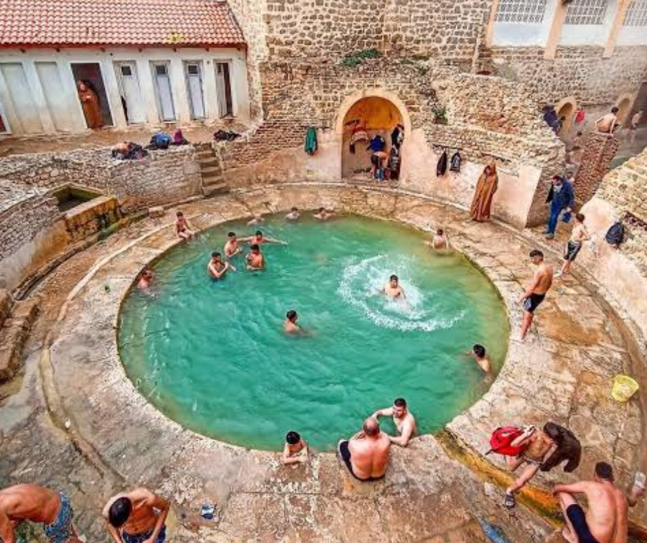 Swimmers in a round open-air thermal pool with stone arches