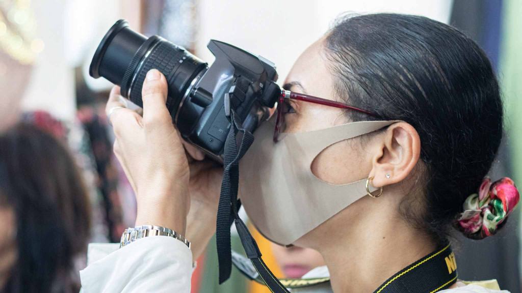 Woman wearing a face mask and pointing a Nikon camera